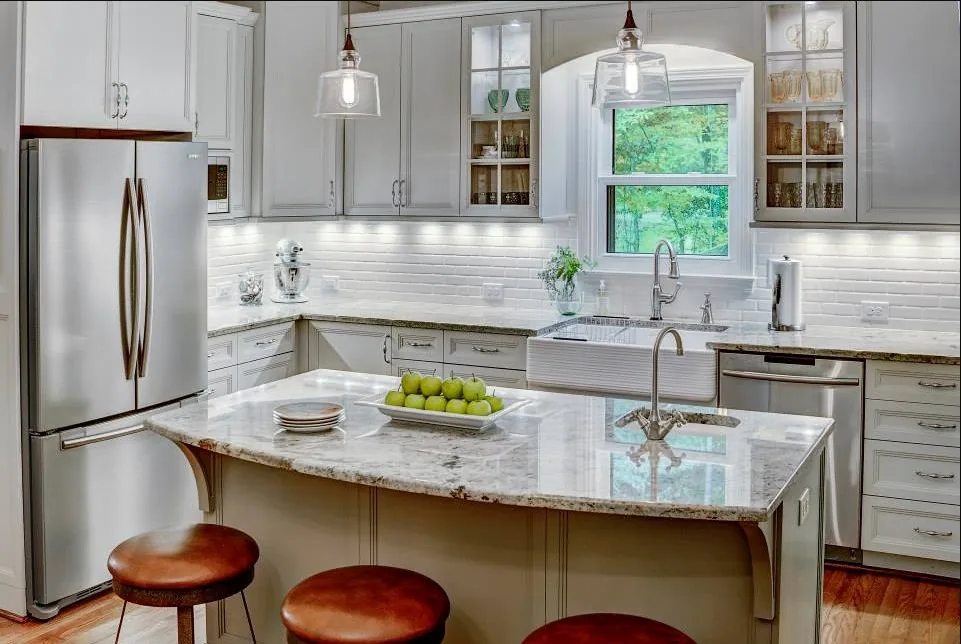 Remodeled kitchen with a marble island, white cabinetry, and pendant lighting