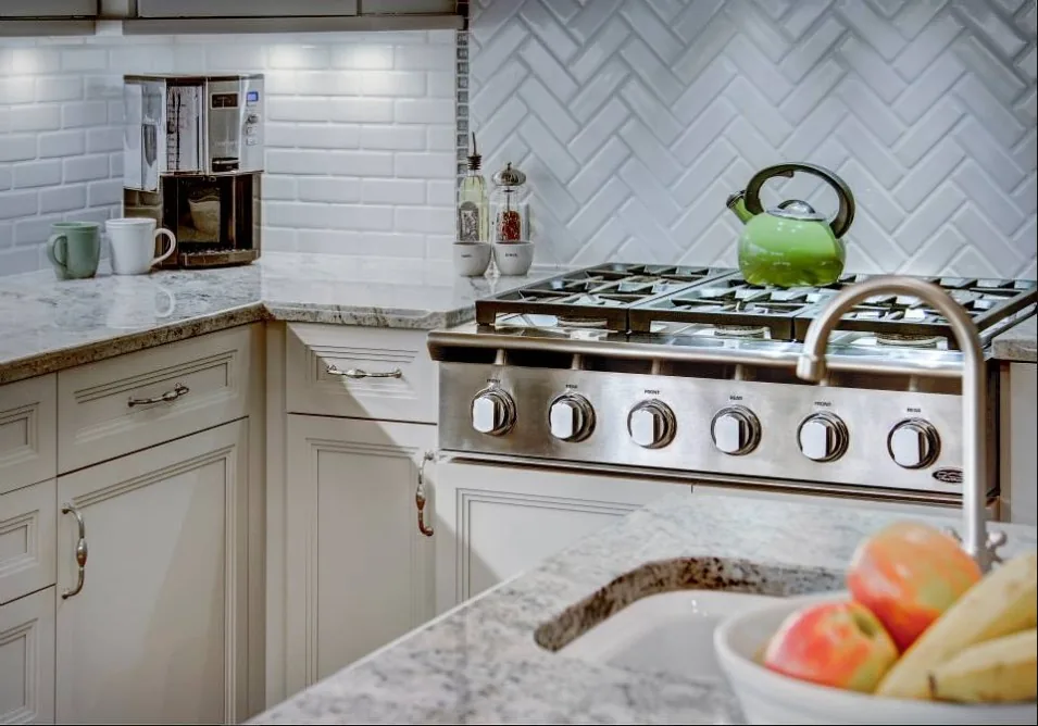 Kitchen range set into a herringbone tile backsplash beside marble counters